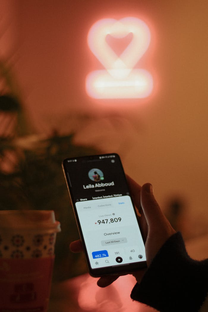 Smartphone display with neon heart backdrop, showcasing modern technology in a cozy setting.